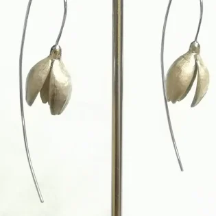 Silver snowdrop drop earrings hanging from stand